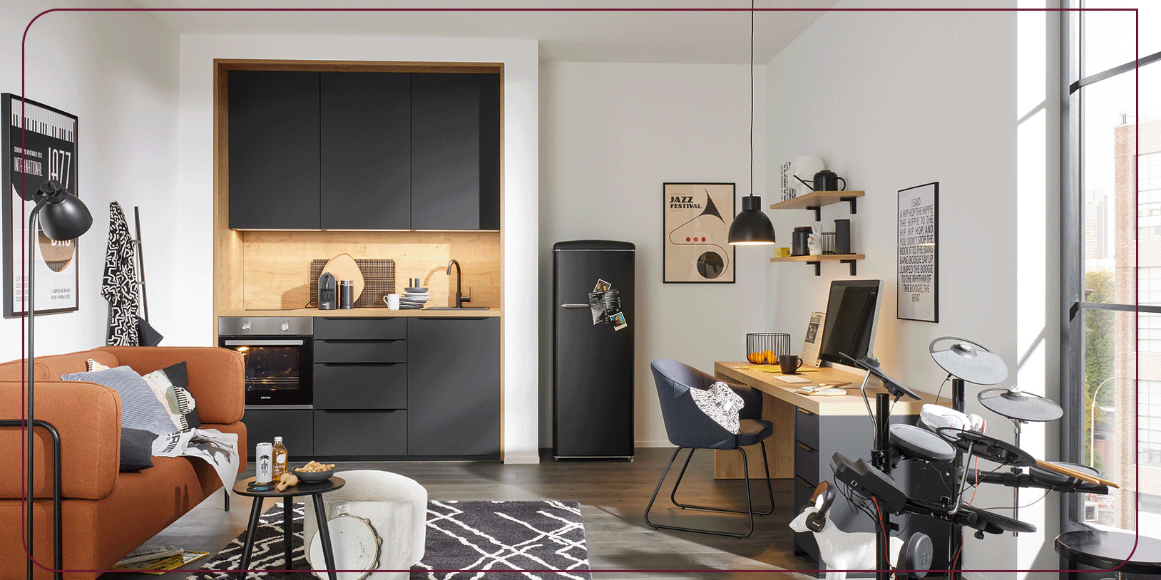 Modernes Studio-Apartment mit einer kleinen schwarzen Küche, einem orangefarbenen Sofa, einem Schlagzeug, einem Schreibtisch mit Computer und Wandregalen. Durch das große Fenster fällt viel Tageslicht herein. Stilvolle Einrichtung, die eine gemütliche und aufgeräumte Atmosphäre vermittelt.